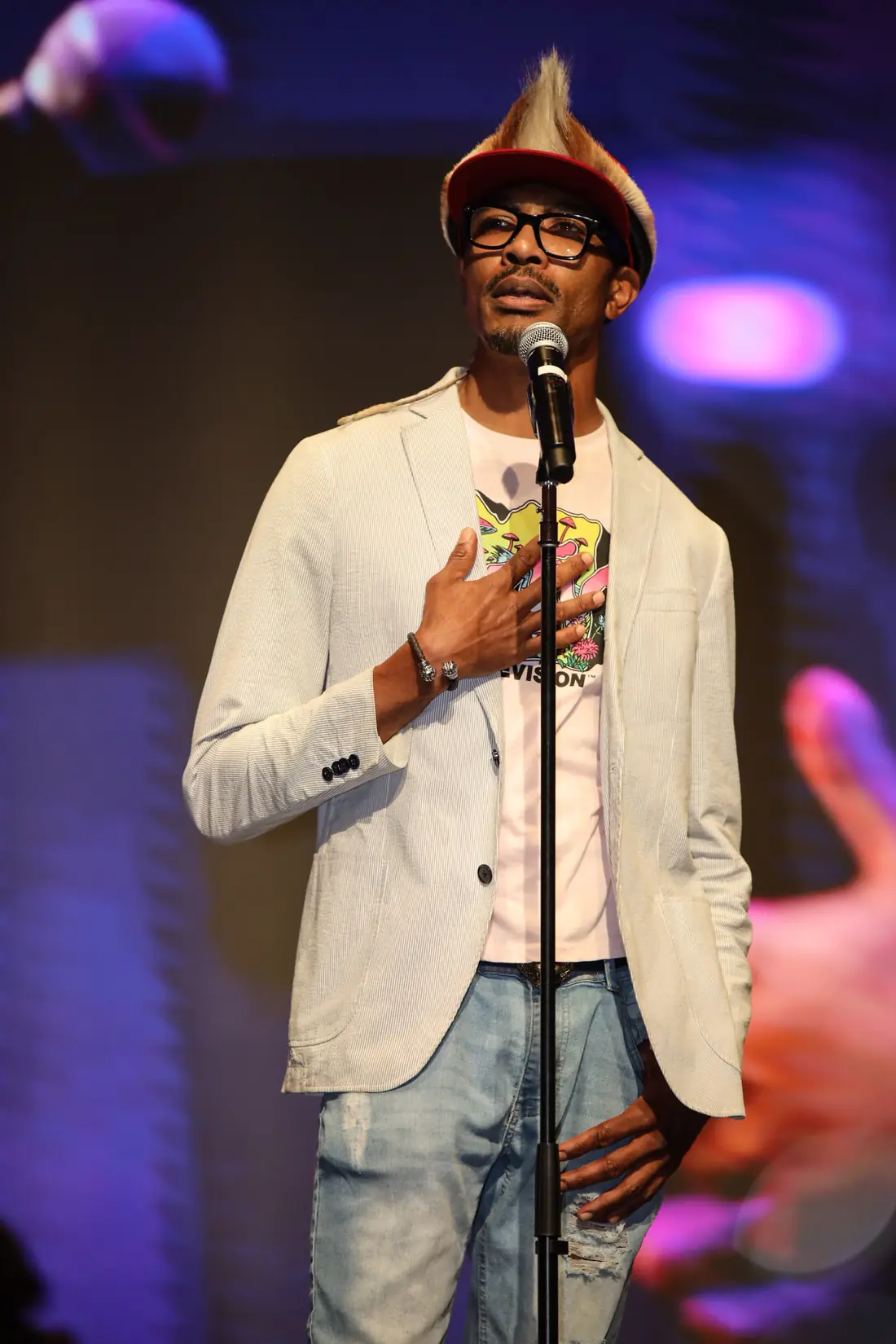 A poet in a tall hat and light blazer performing at the mic