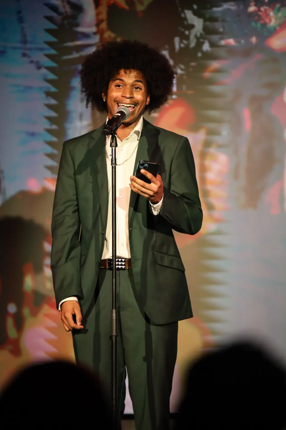 An open mic performer in a green suit at the mic, phone in hand